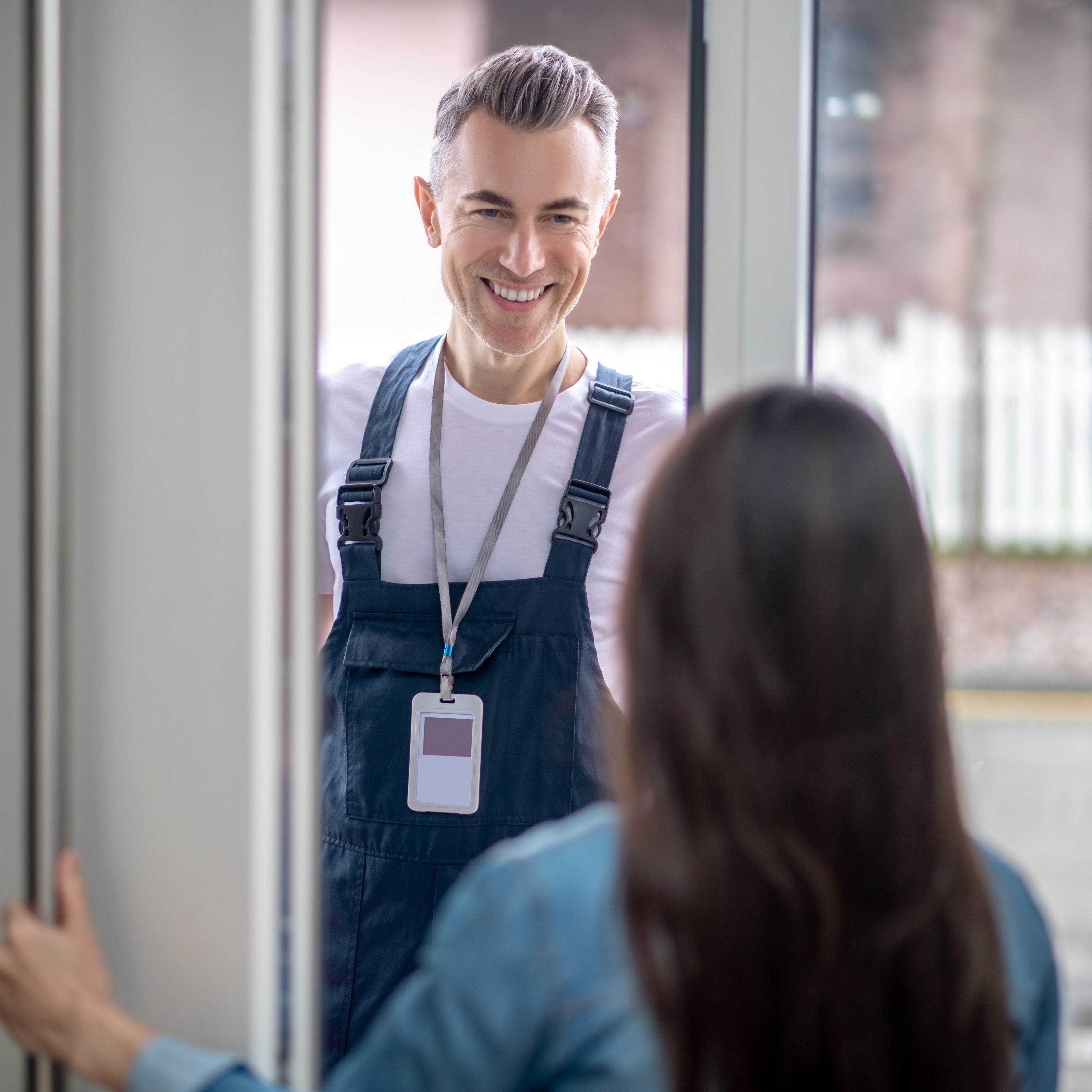 Man in overalls standing in a glass door with a woman, likely a service provider or repairman.